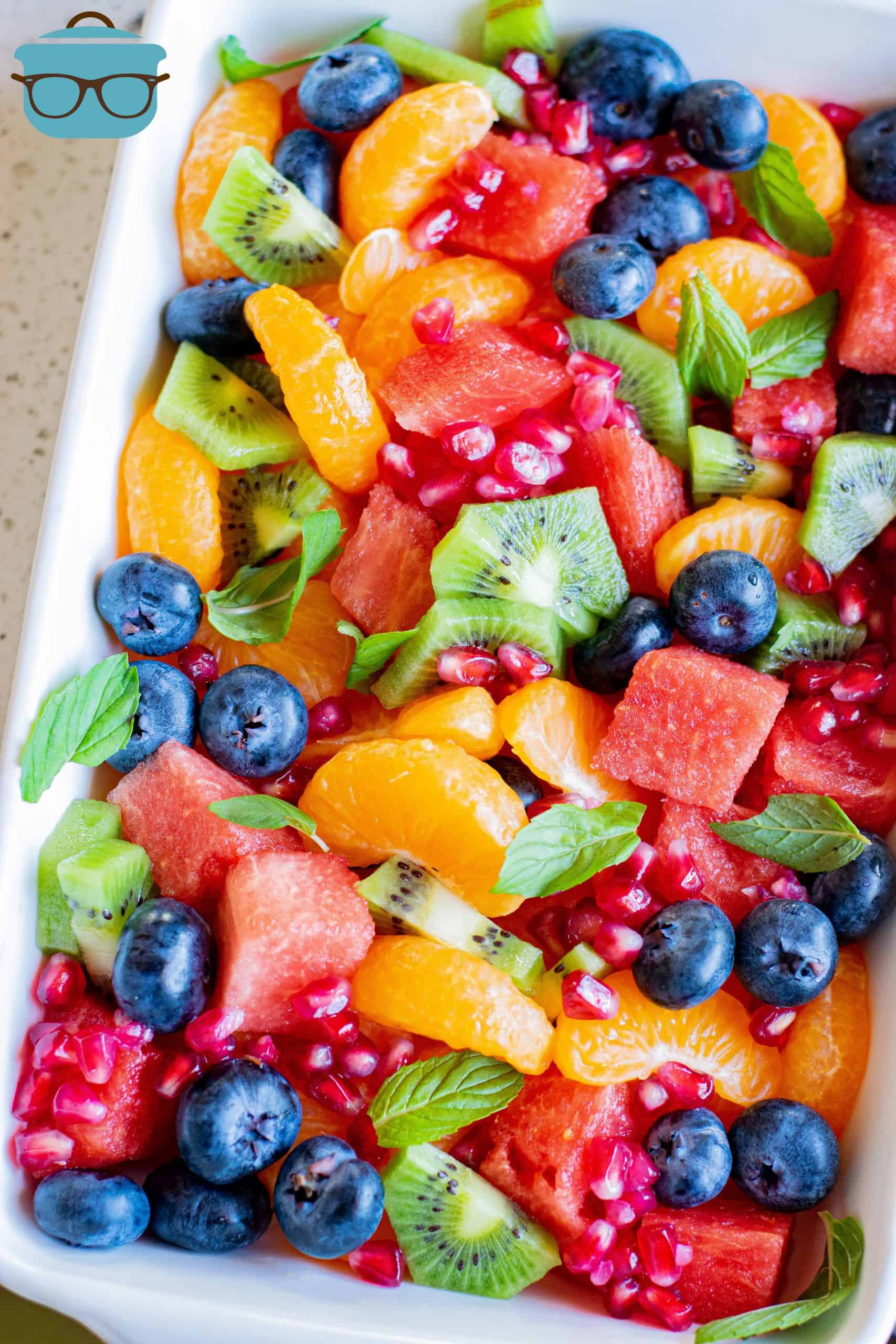 The Best Fruit Salad in large white dish with fruit mixed together and garnished with mint leaves.