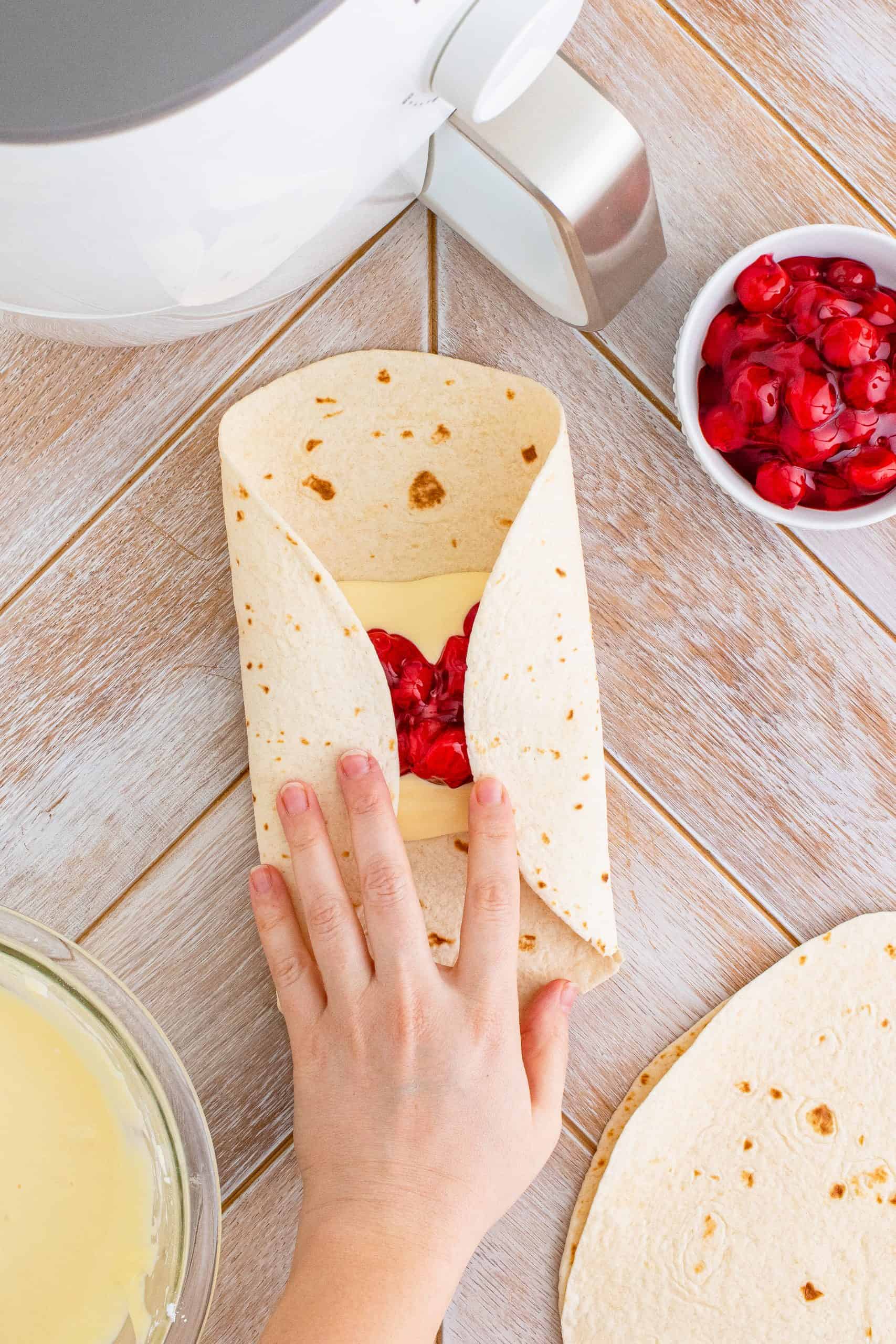 Hand folding over two sides of of tortilla over filling.
