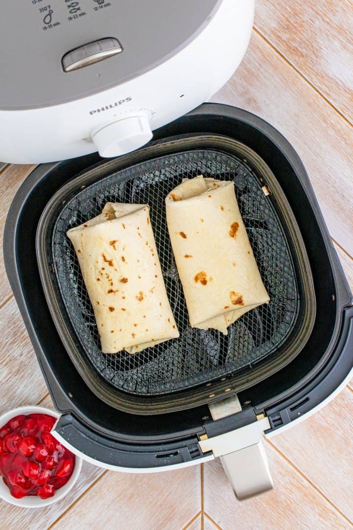 Two Chimichangas in air fryer basket.