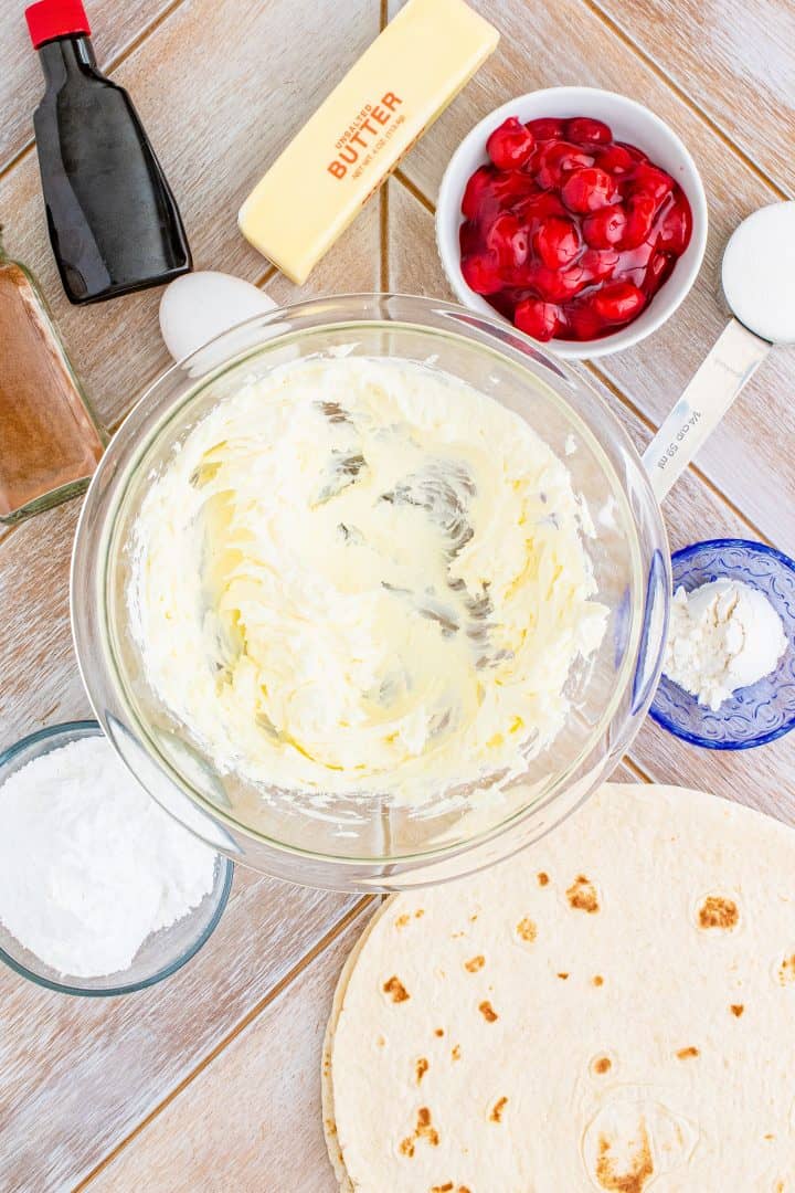 Beaten cream cheese in bowl with ingredients surrounding it.