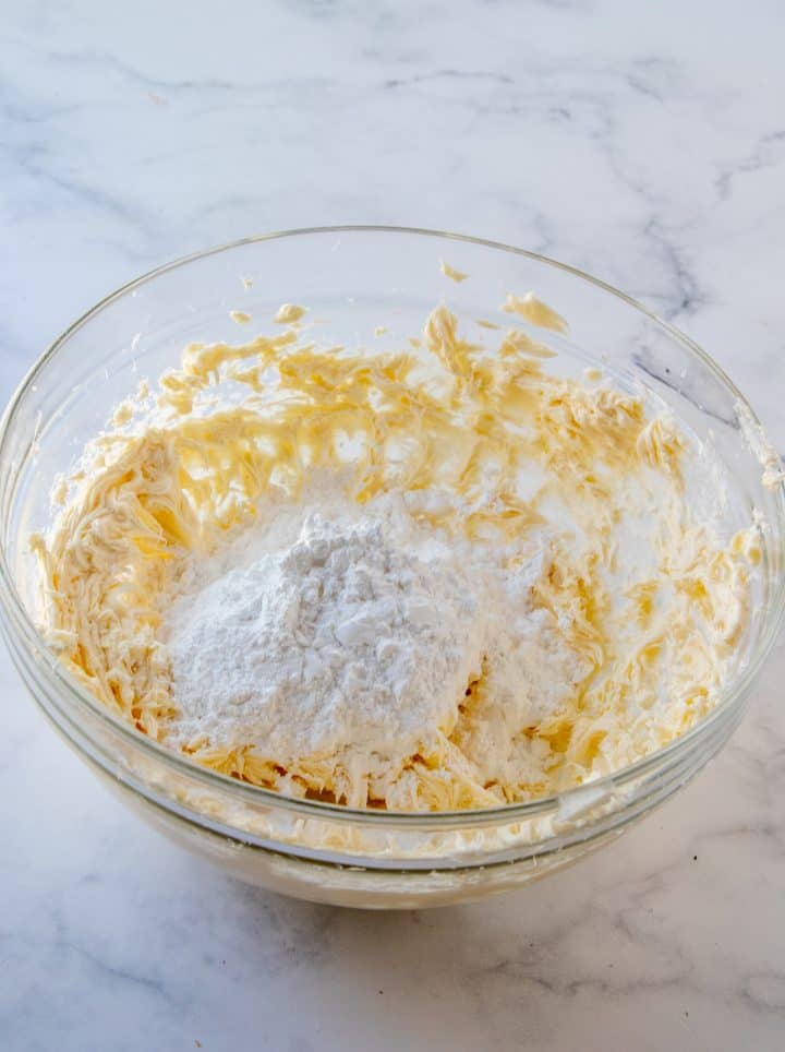 Powdered sugar added to butter mixture in clear bowl.