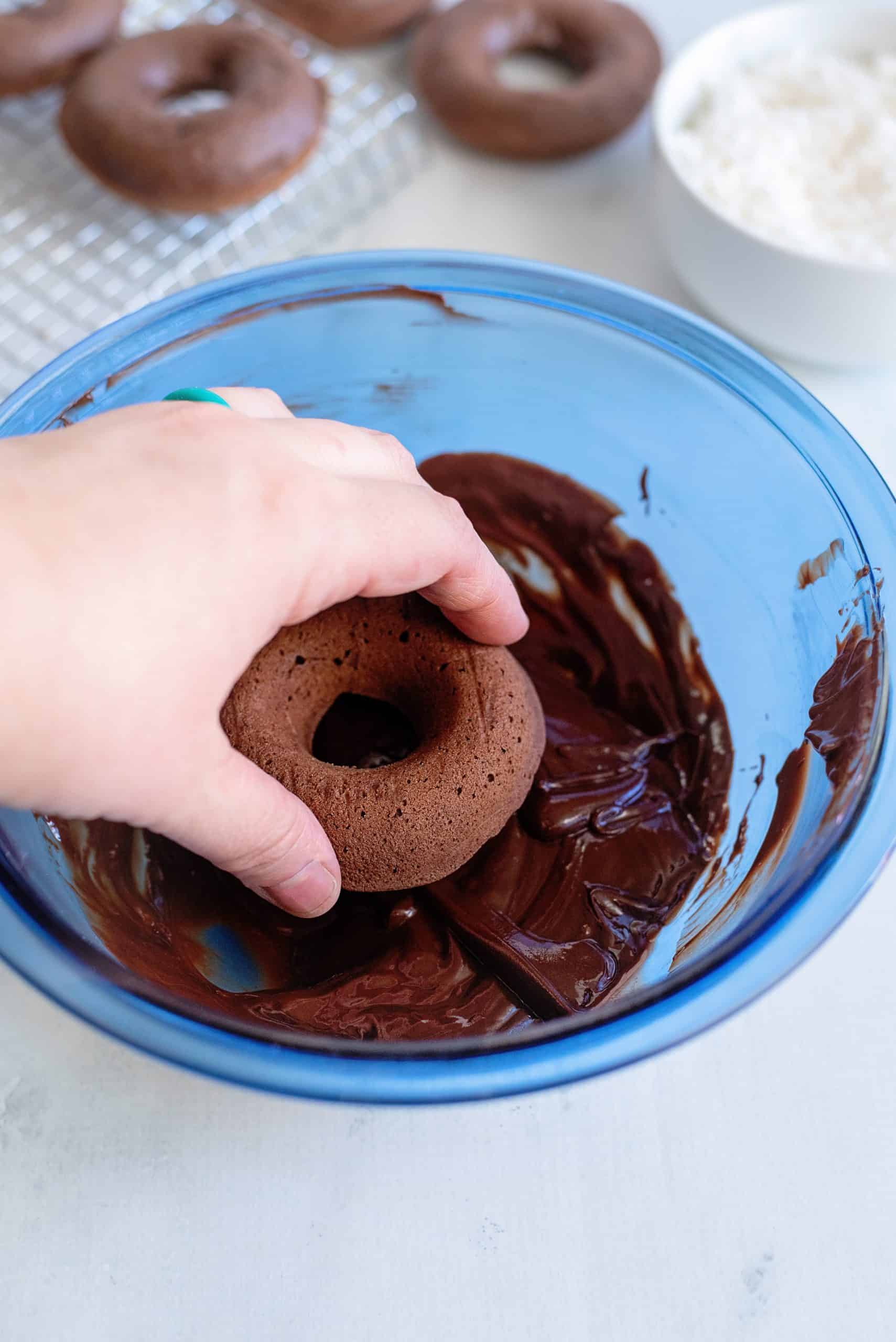 Hand dipping baked donut into chocolate