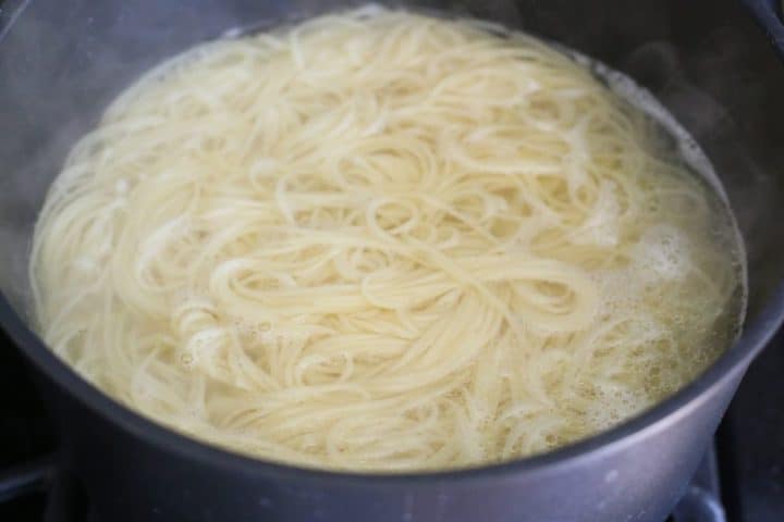 angel hair pasta cooking in water in a large black pot