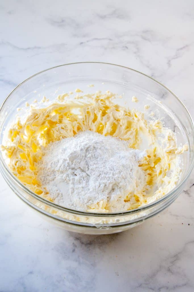 Powdered sugar added to butter mixture in clear bowl
