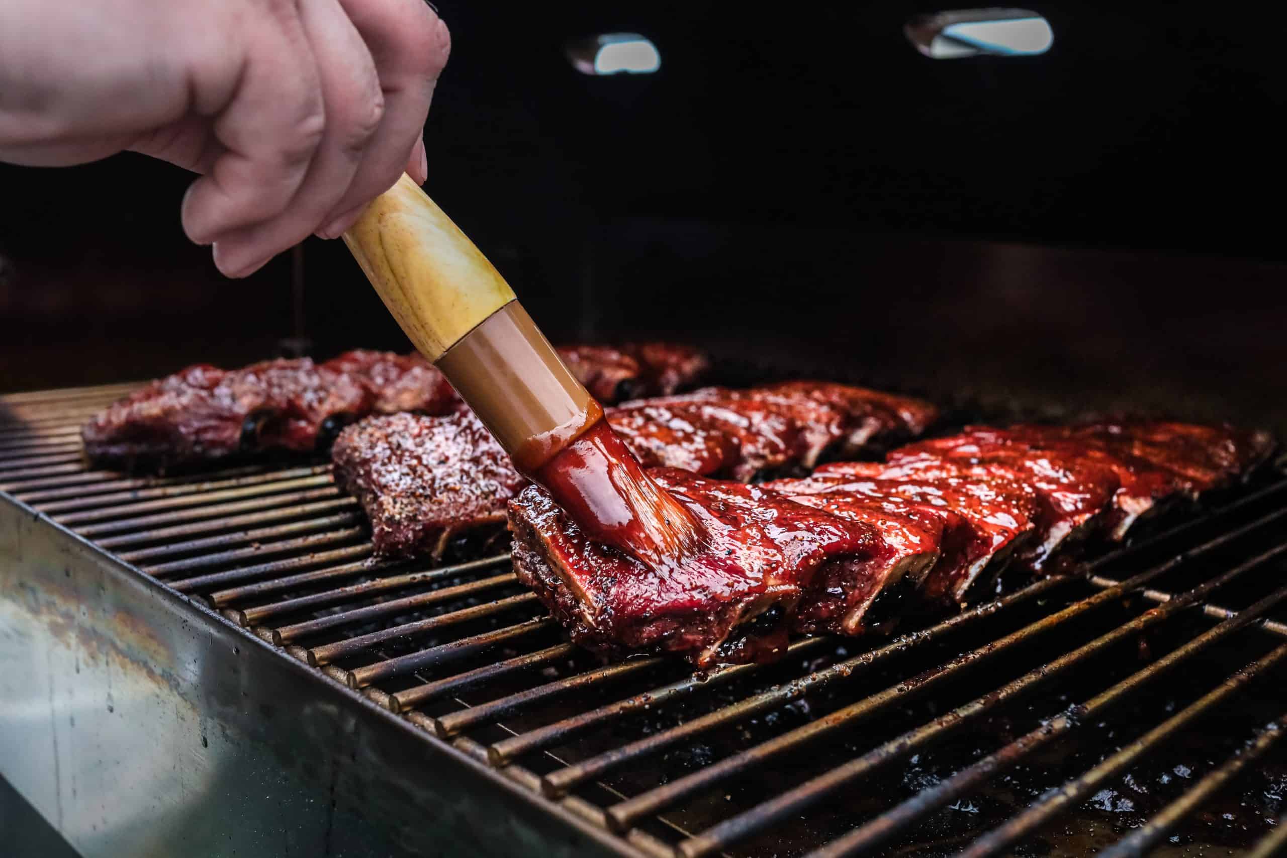 Ribs being brushed with BBQ sauce on smoker.