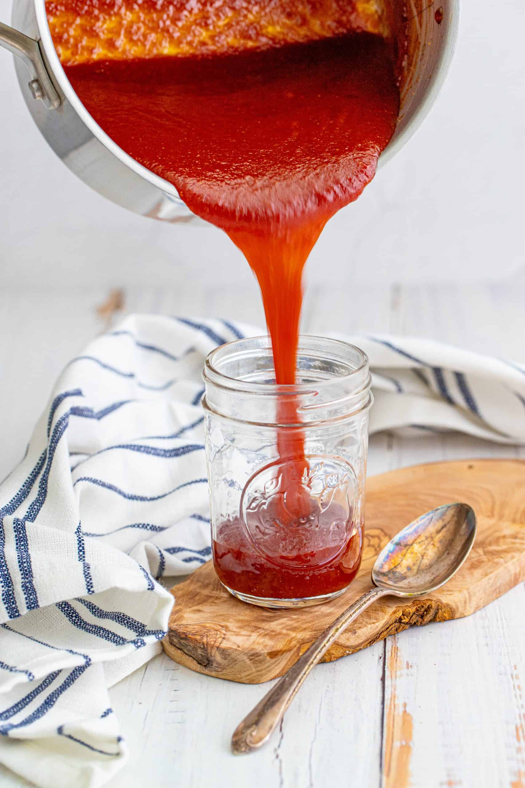 BBQ Sauce being poured into jar on wooden board with spoon