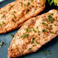 Square image close up of finished Air Fryer Chicken Breasts on gray plate topped with parsley
