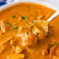 Close up square image of white bowl filled with Creamy Butter Chicken with spoon in bowl