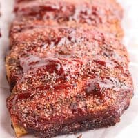 Square image of finished Smoked Beef Ribs uncut on parchment paper with BBQ Sauce