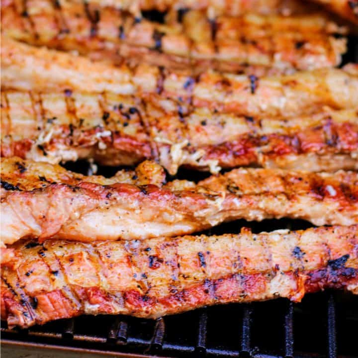 Strips of the Smoked Pork Belly Recipe on smoker showing char marks square image