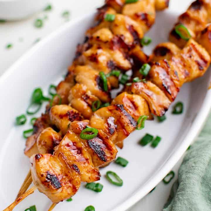 Square photo of Teriyaki Chicken Skewers on white platter with green onions