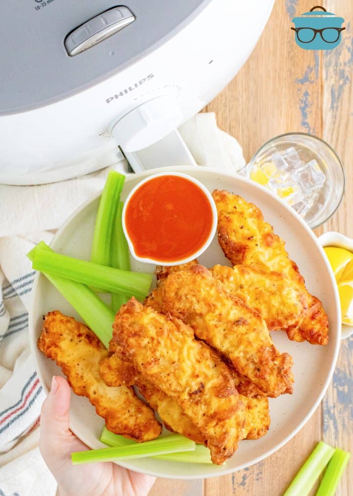 Air Fryer Chicken Crispers on plate with celery and dipping sauce being held by hand