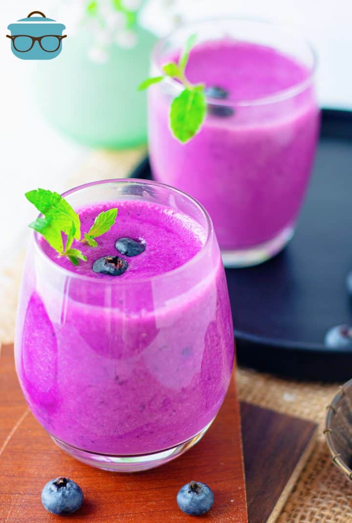 Two Blueberry Smoothies on wooden platter garnished with blueberries and mint
