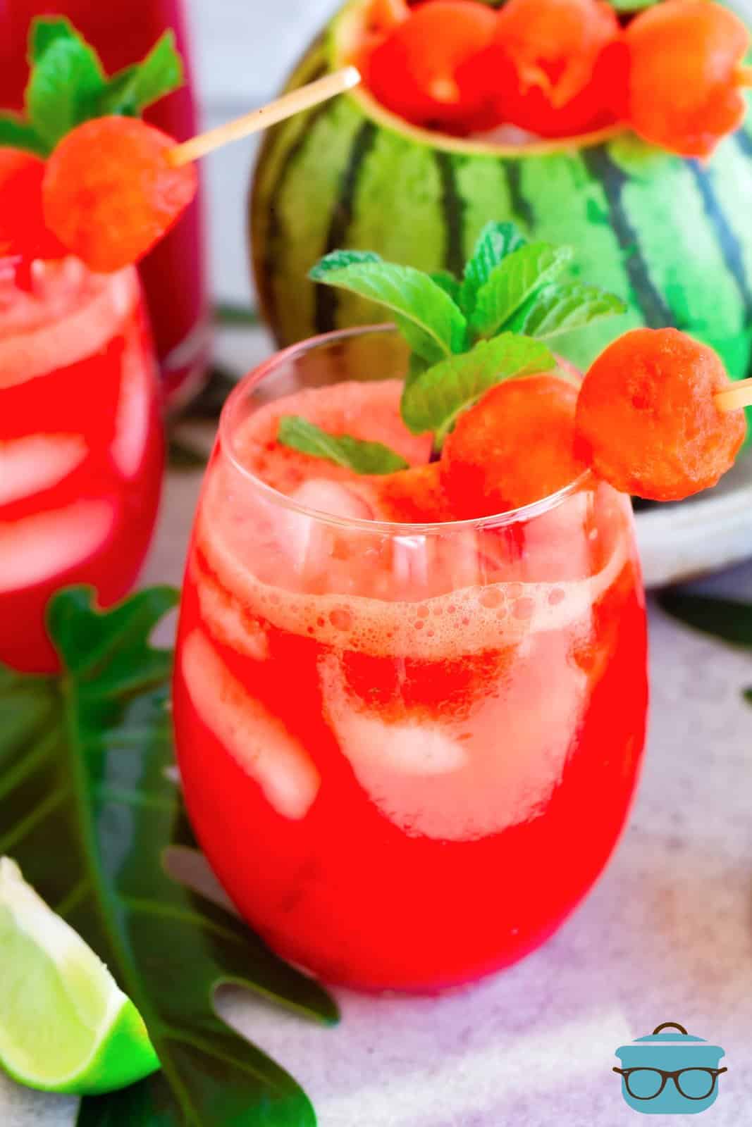 a wine glass holding watermelon margarita mix with a twig of basil on the rim.