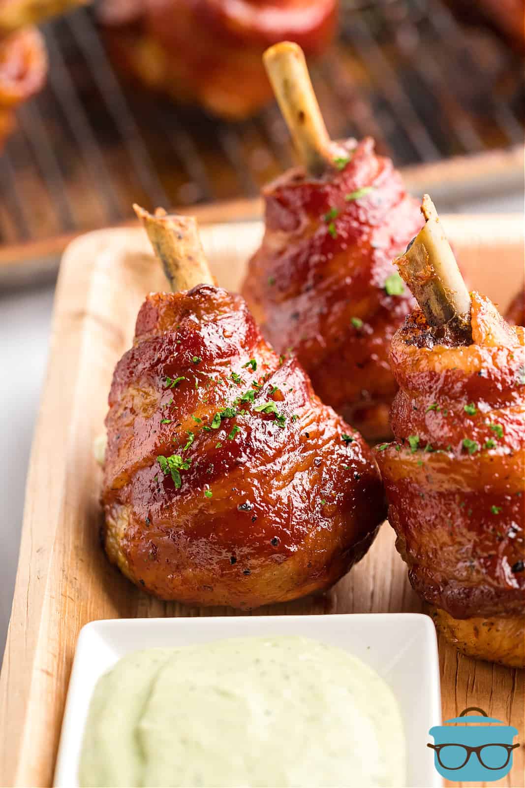 Smoked Bacon Wrapped Chicken Lollipops in dish next to dipping sauce.