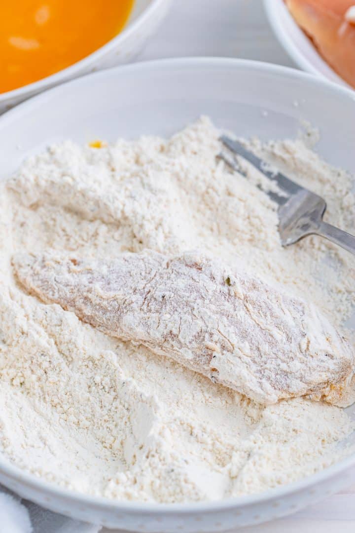 Chicken tender being dipped back into flour mixture after being dipped in egg mixture