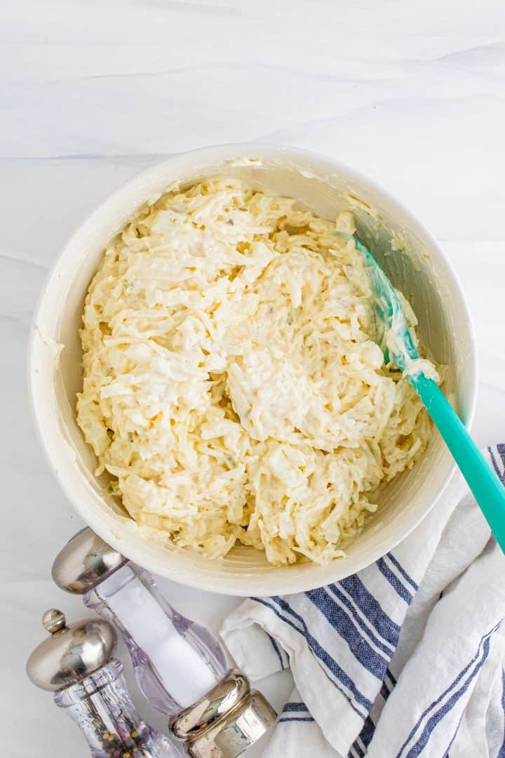 hash browns stirred together with sour cream mixture in a white bowl with a blue spoon