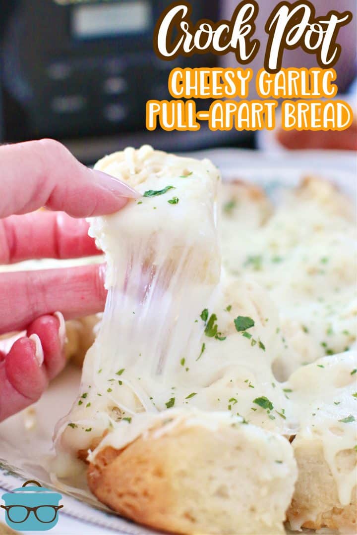 Crock Pot Cheesy Garlic Pull Apart Bread recipe from The Country Cook, photo of a hand pulling a piece of cheese bread off a plate