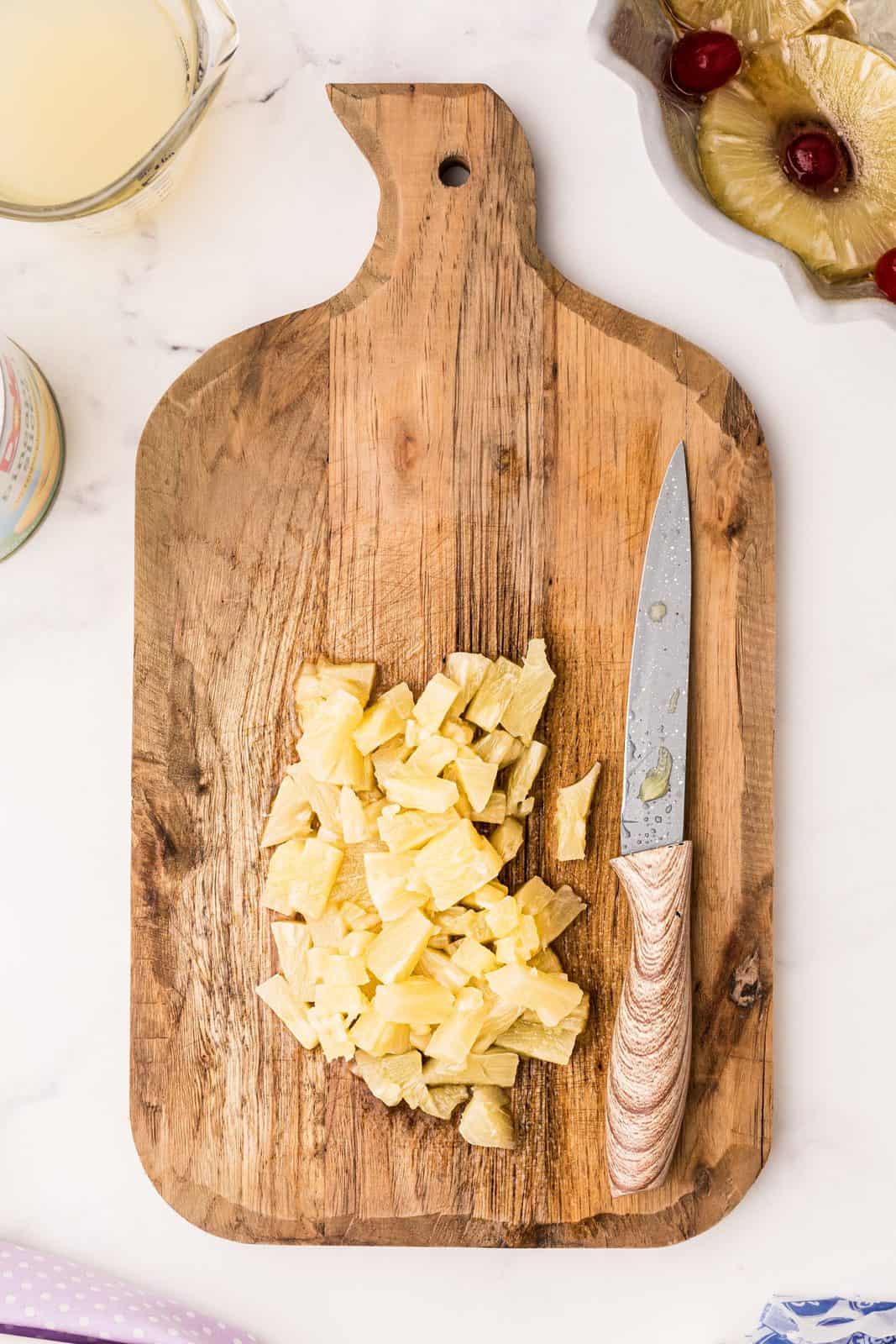 Chopped up pineapple rings on wooden cutting board.