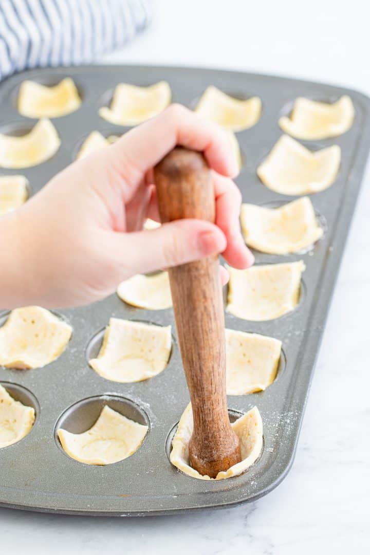 Cut puff pastry being pressed into mini muffin tin