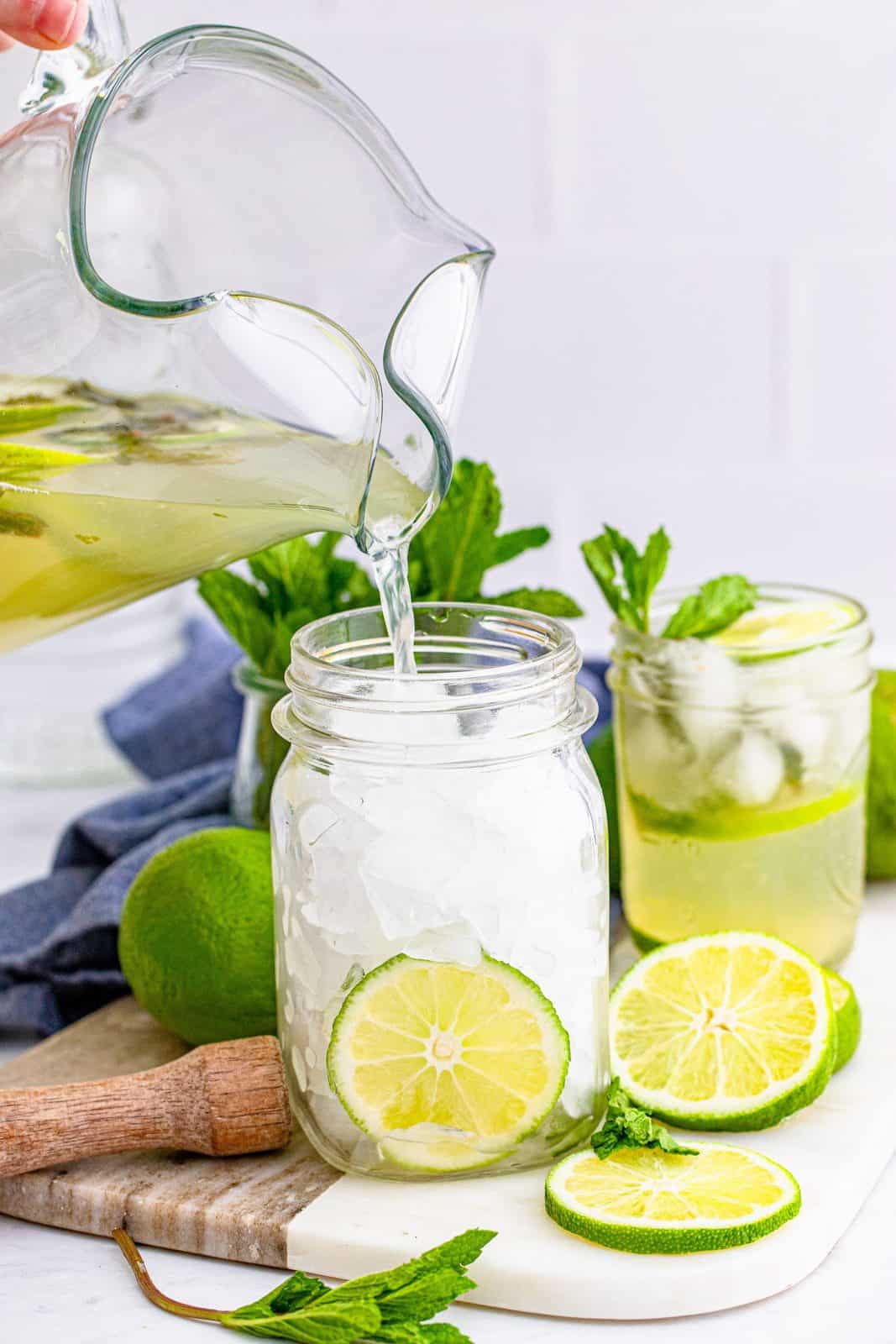 Pitcher pouring Summer Mojito Recipe into mason jar that is filled with ice.