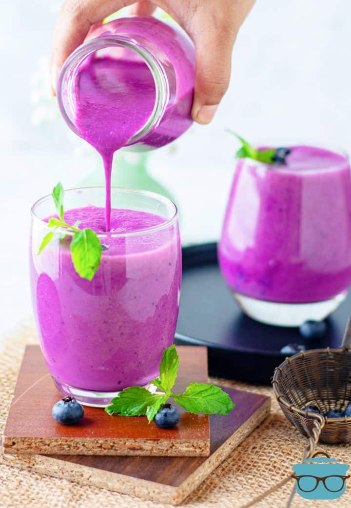 Hand pouring Blueberry Smoothie mixture into glass