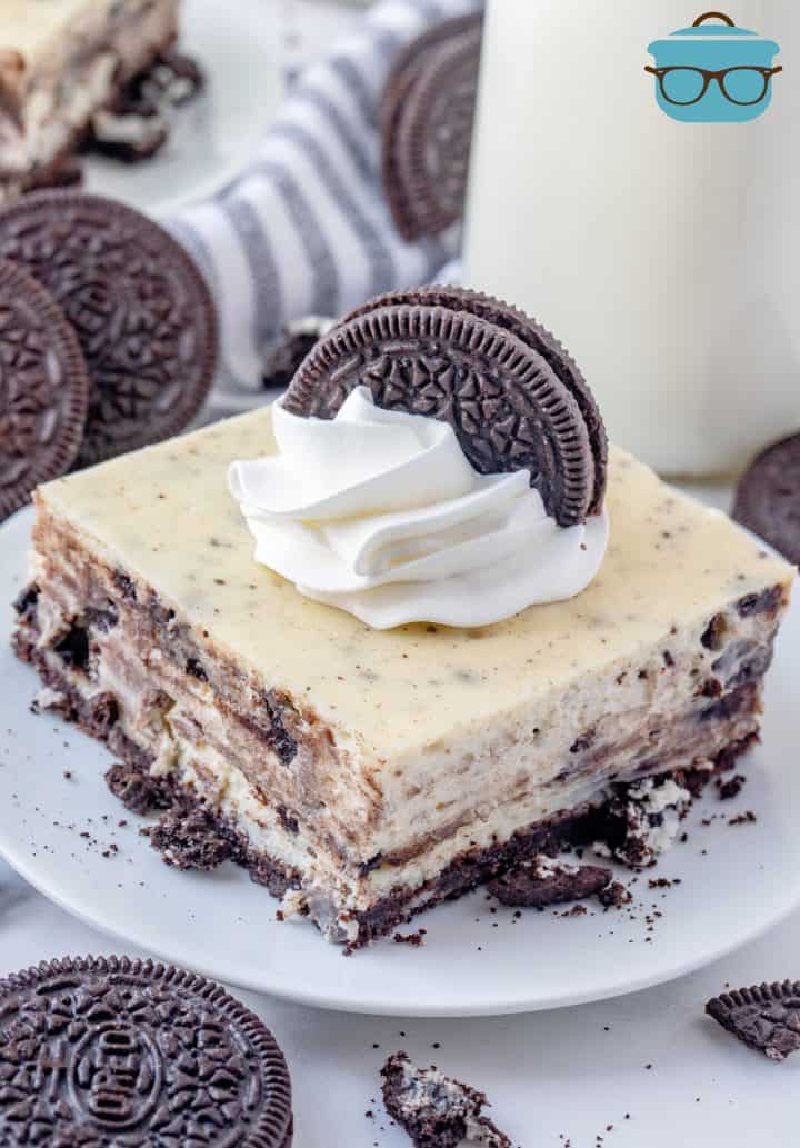 Slice of Oreo Cheesecake Bars on white plate topped with whipped topping and oreo cookie.