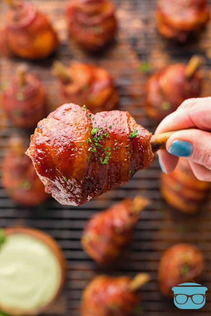 Hand holding up one Smoked Bacon Wrapped Chicken Lollipop