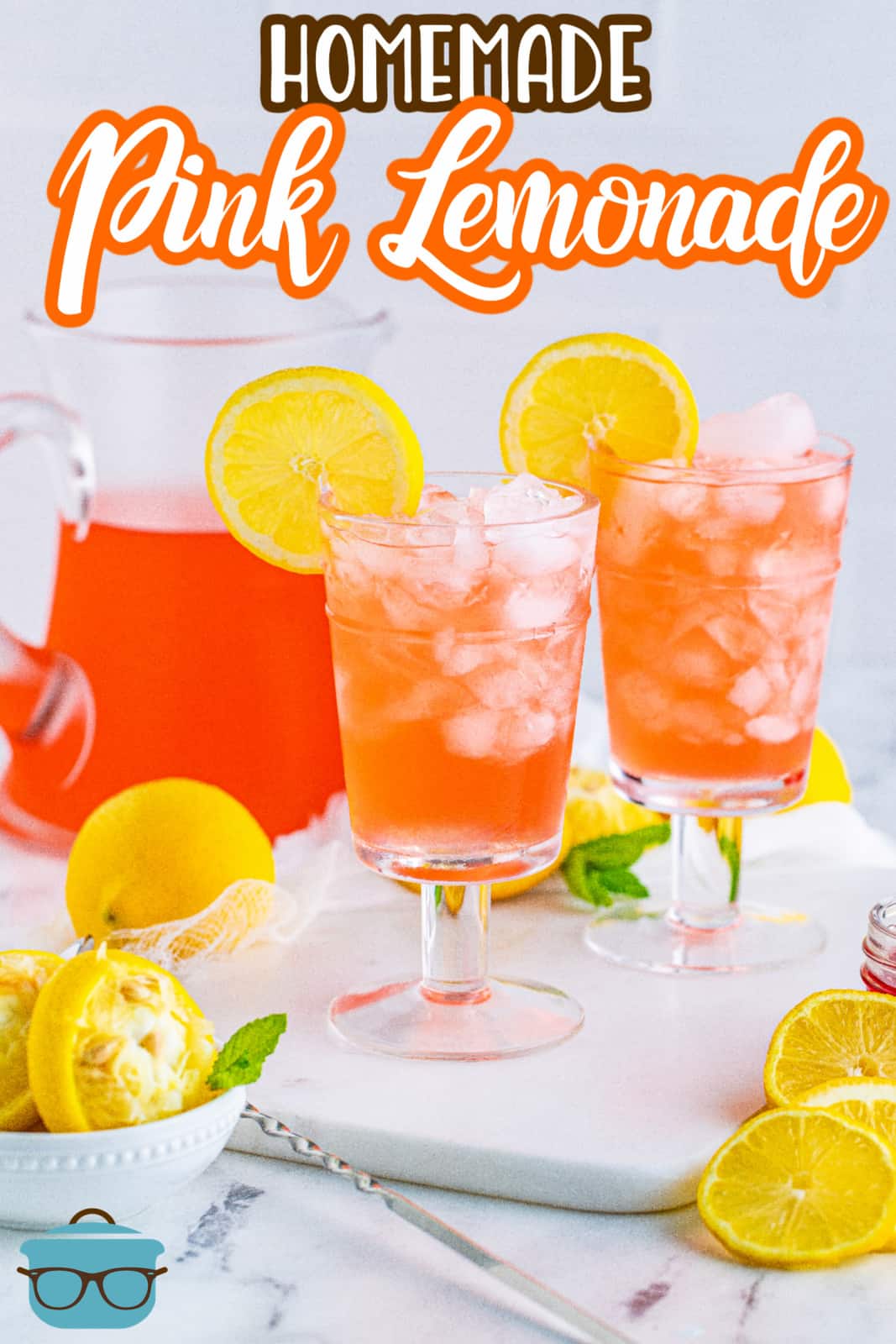 Two glasses of Homemade Pink Lemonade on white platter garnished with lemon with pitcher in background.