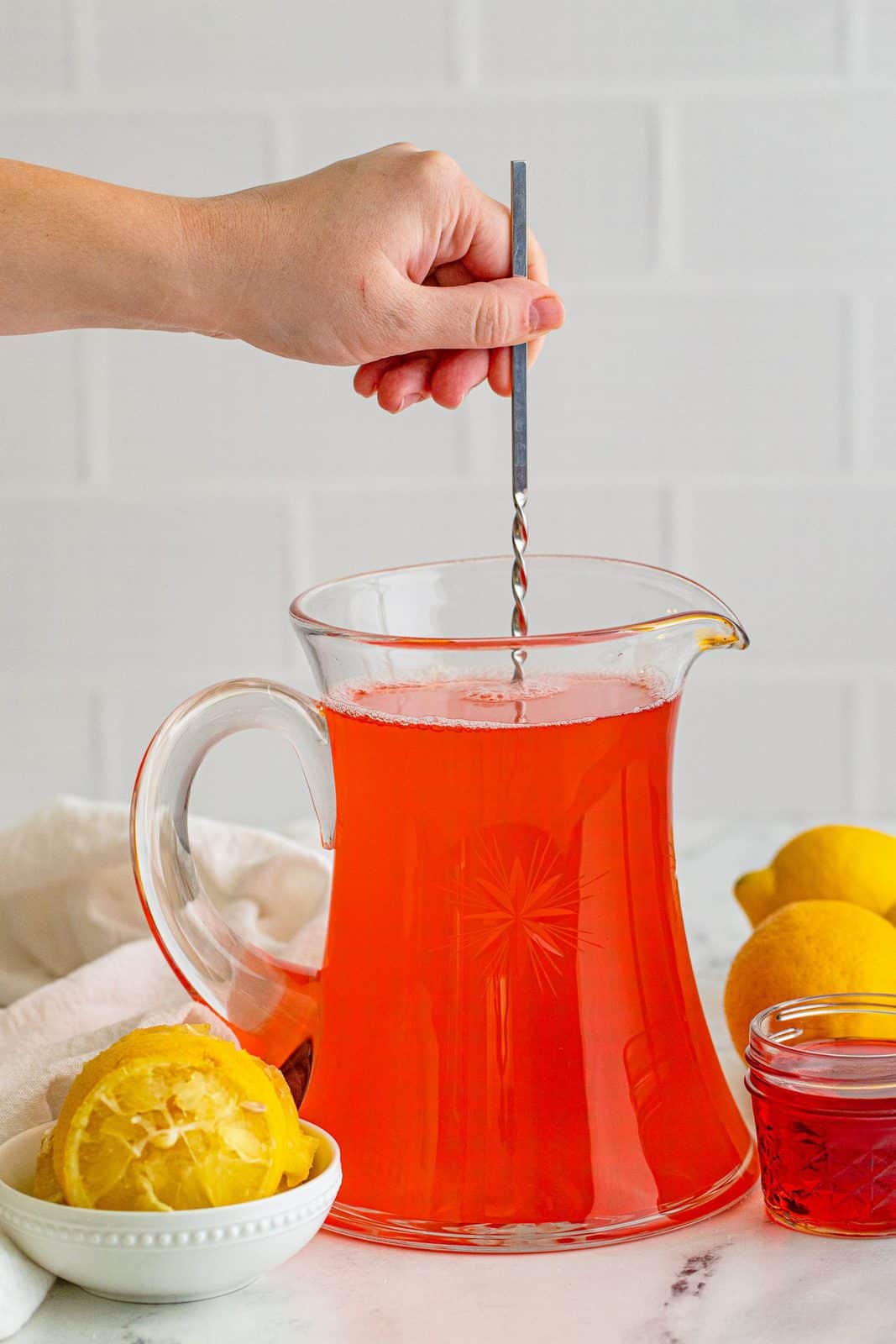 Hand stirring up Homemade Pink Lemonade Recipe in pitcher.