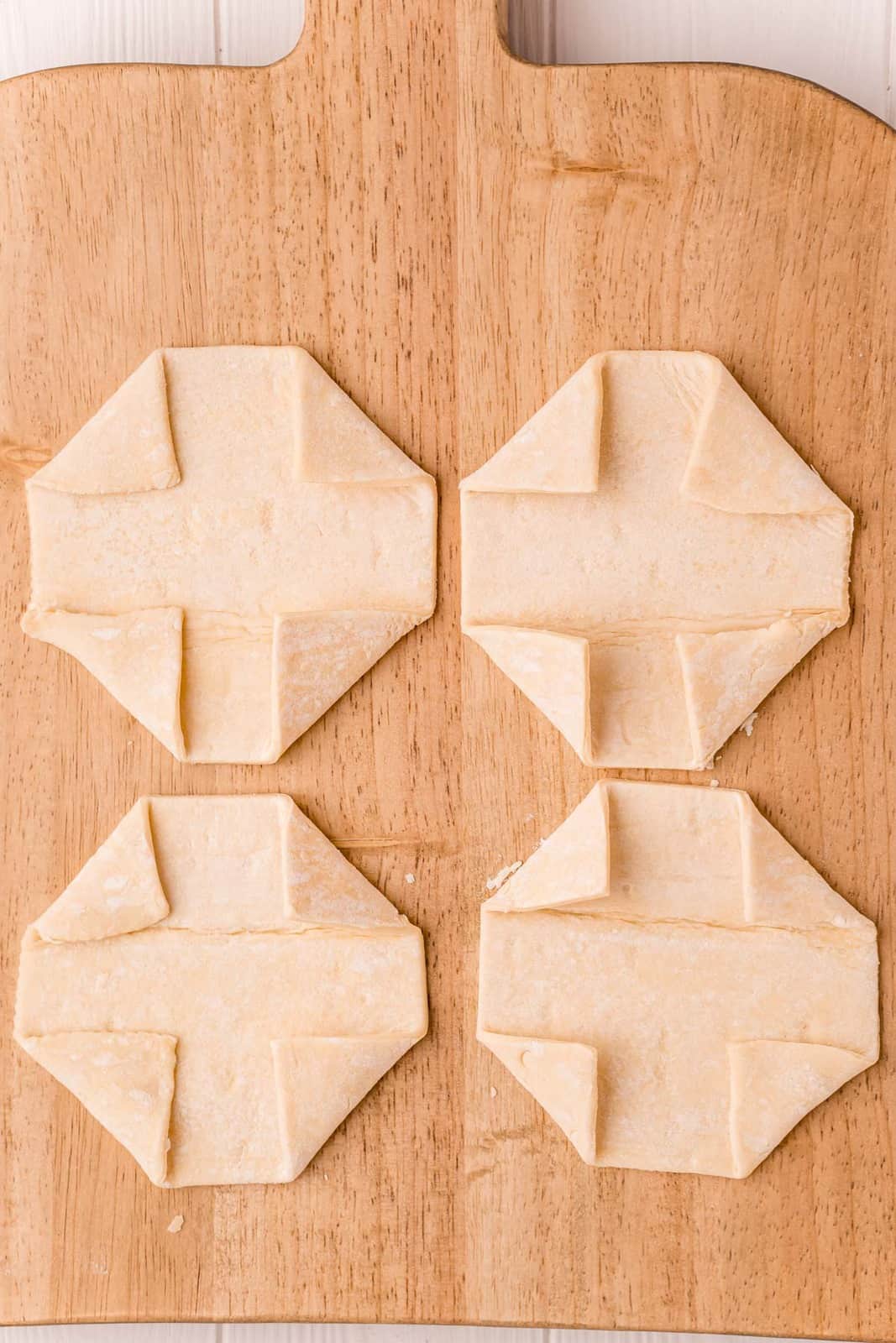 Puff pastry squares with edges folded in on wooden cutting board