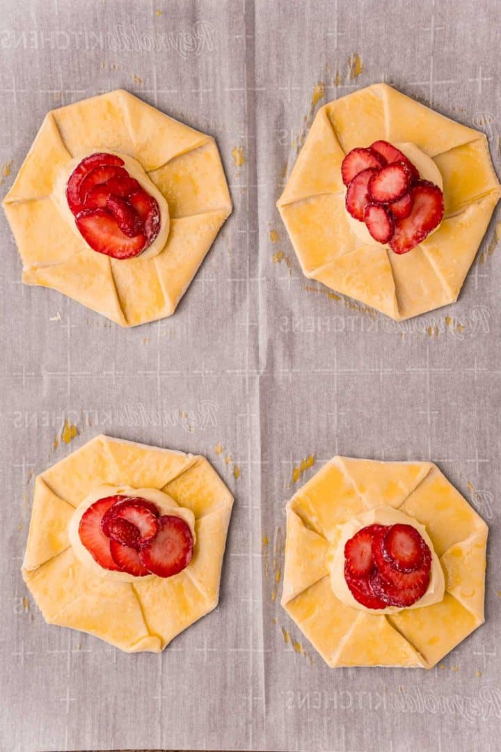 Unbaked danishes topped with strawberries and cream cheese mixture on parchment paper lined baking sheet