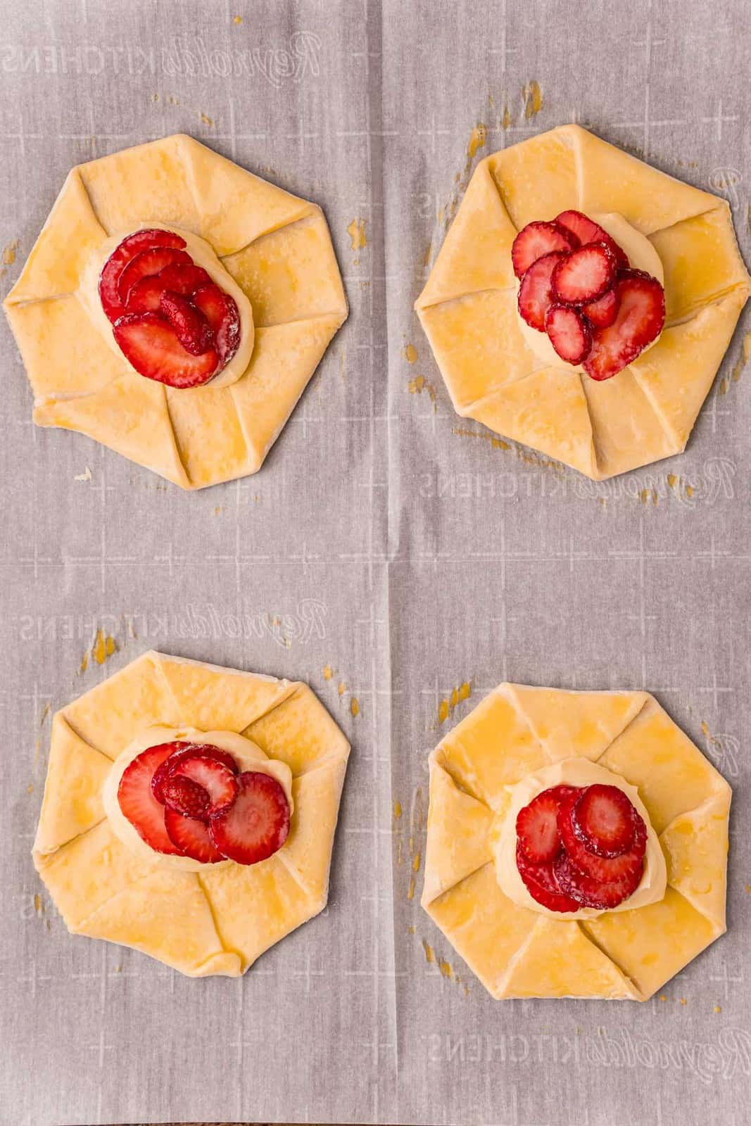 Unbaked danishes topped with strawberries and cream cheese mixture on parchment paper lined baking sheet