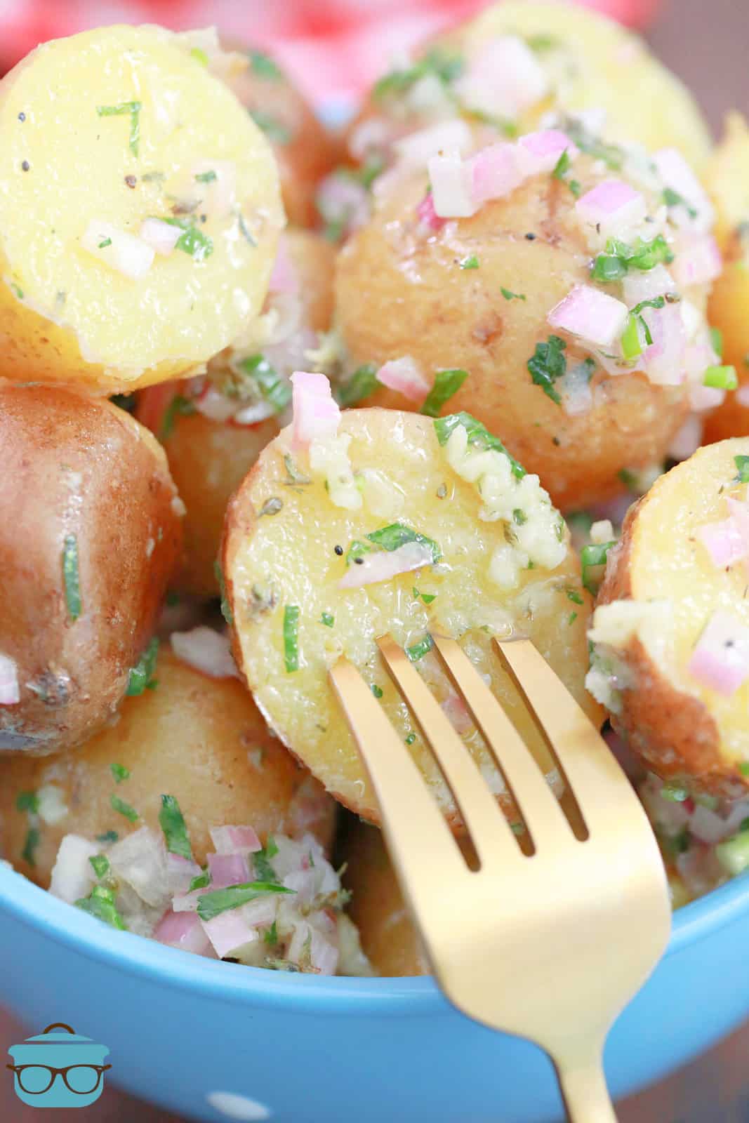 a fork poking into a potato that is covered in an herb vinaigrette. 