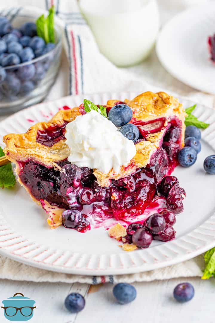 slice of Homemade Blueberry Pie on a white plate with a dollop of whipped cream on top.
