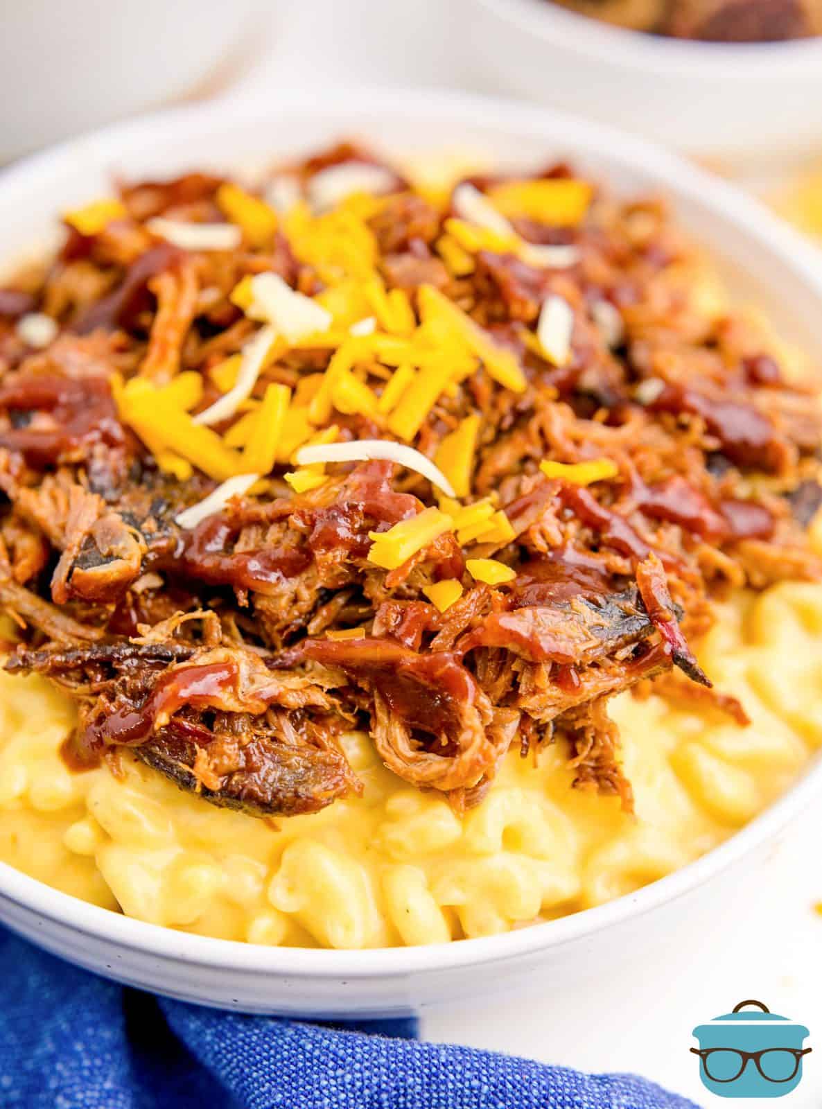 Pulled Pork Macaroni and Cheese in a white bowl topped with shredded cheese.