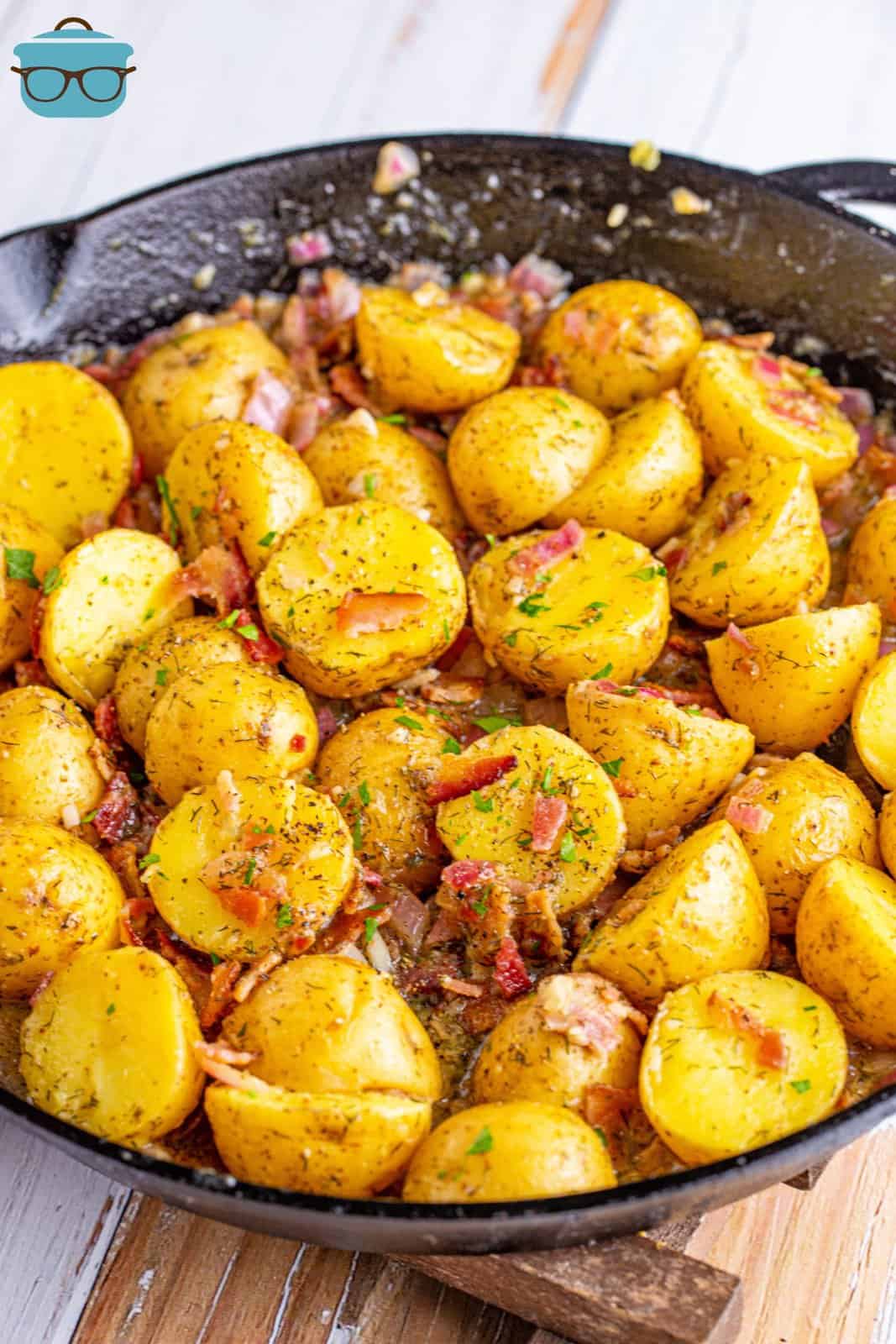 a large cast iron skillet with fully cooked warm bacon potato salad with some fresh chopped parsley sprinkled on top. 