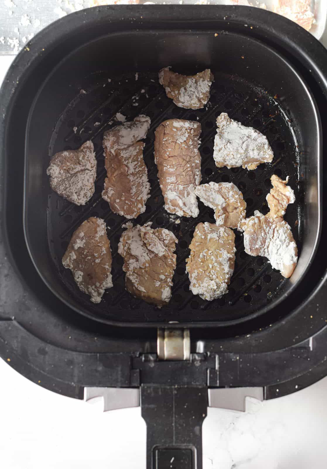 chicken pieces shown (before cooking) in the basket of an air fryer.