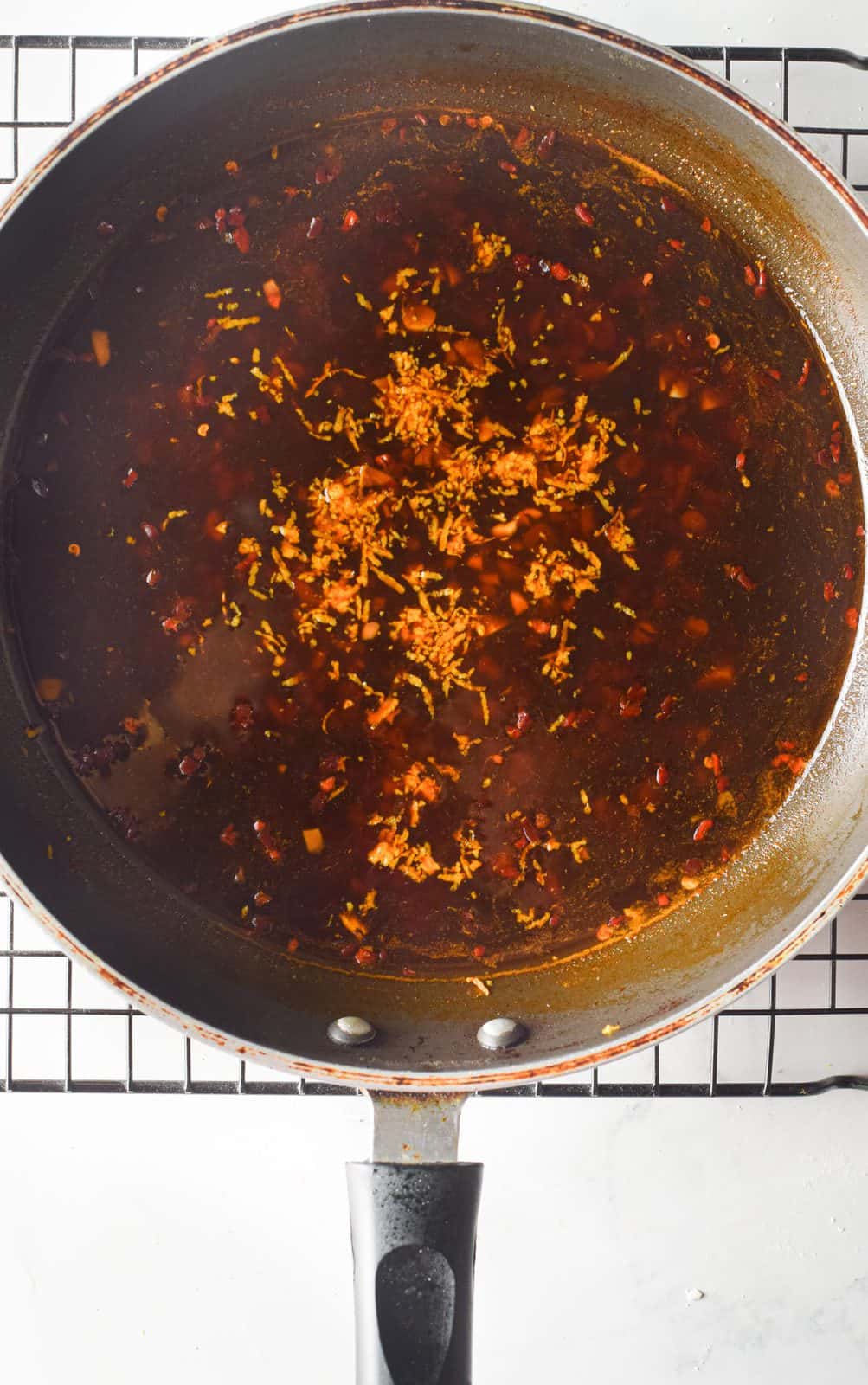 orange zest along with orange sauce shown in a skillet.