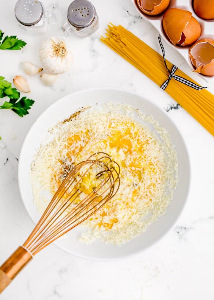 eggs, parmesan cheese, and black pepper being whisked together in a white bowl.