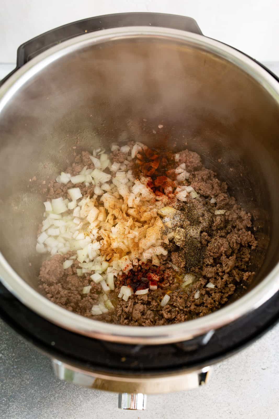 Cooked ground beef in instant pot with onions and dry seasonings added.