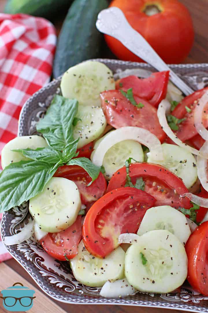 tomato cucumber and onion salad shown in a brown and white Spode serving bowl with fresh cucumbers and a tomato in the background.