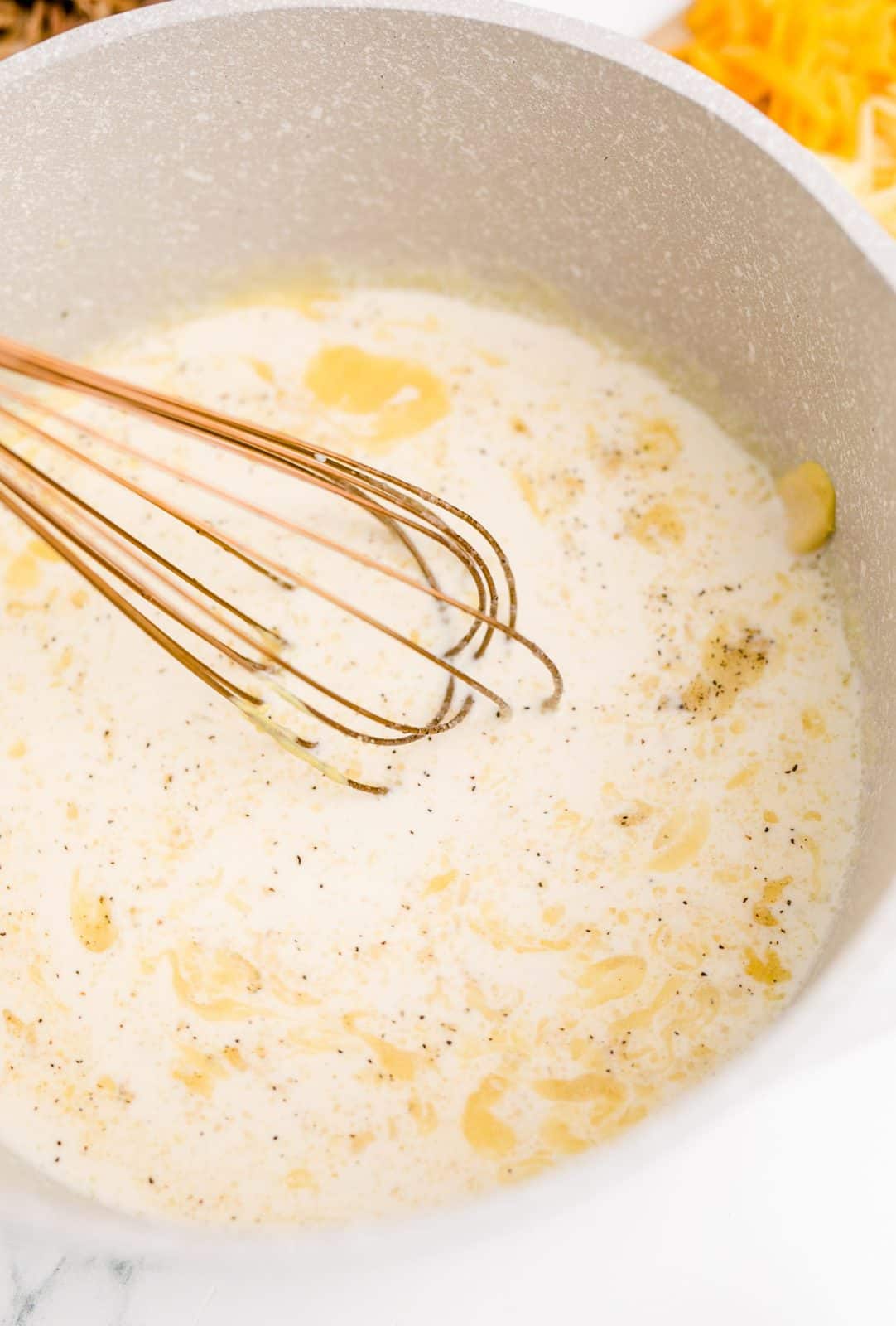 Evaporated milk, chicken broth, salt, pepper, mustard, onion powder, and garlic added to butter and flour mixture with a whisk.
