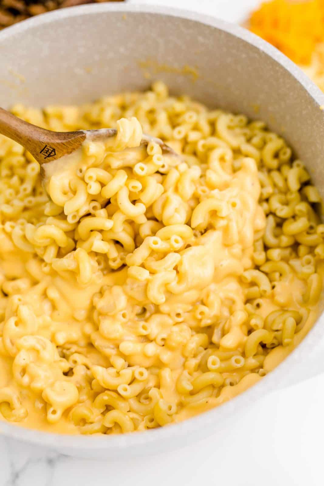 Macaroni added to cheese mixture and being stirred together with a wooden spoon.
