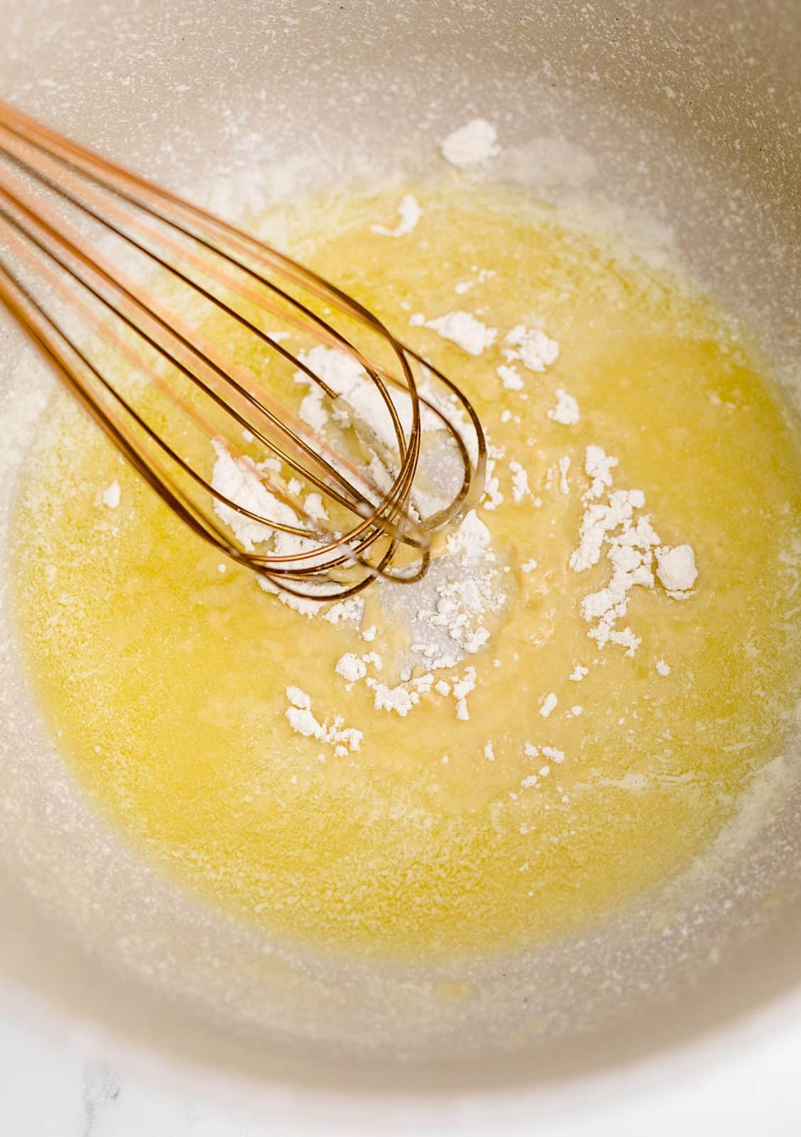 Melted butter with flour added in dutch oven being stirred together by a whisk.