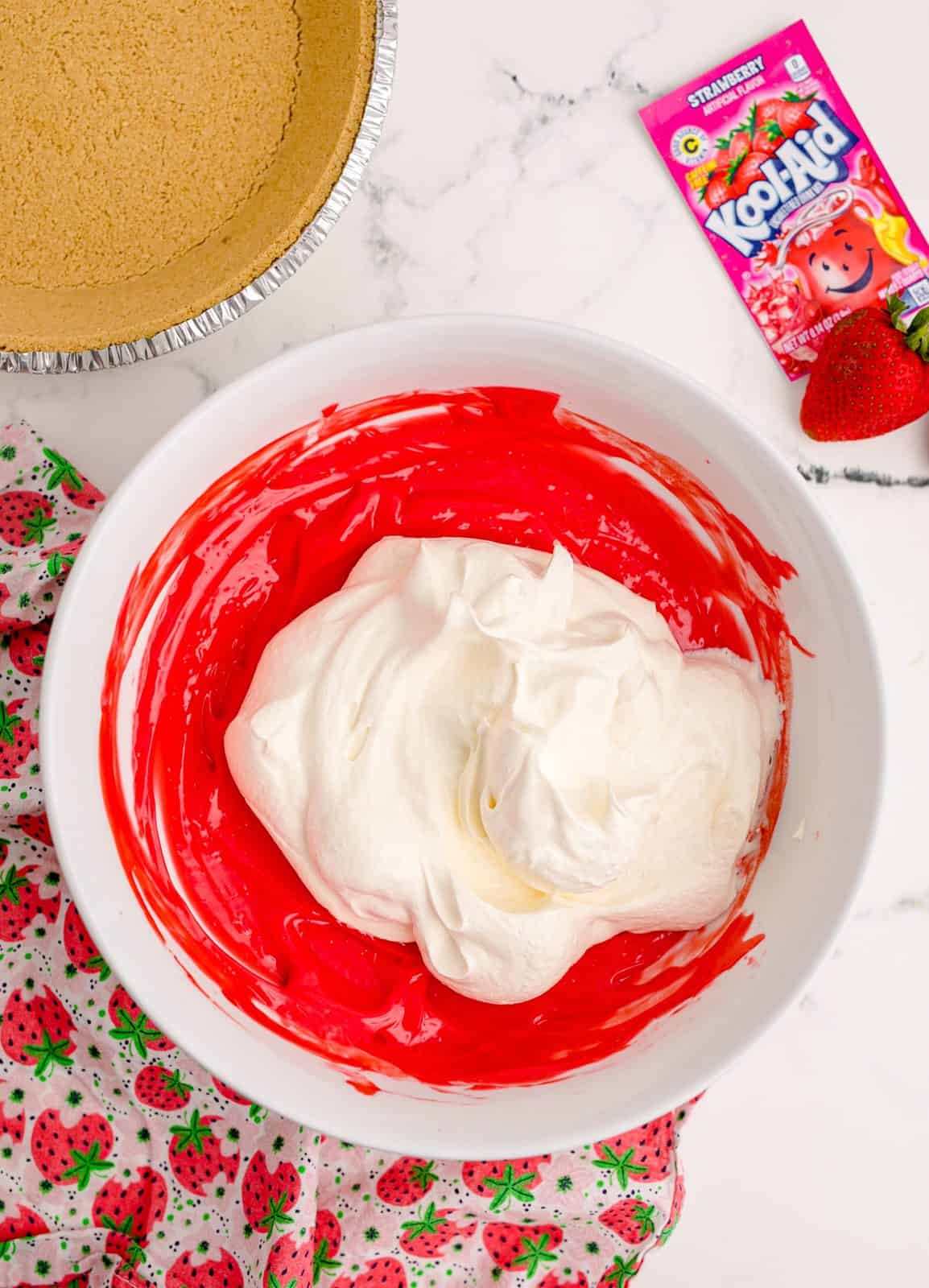 Mixed up Kool-Aid mixture with cool whip added on top in a white bowl.