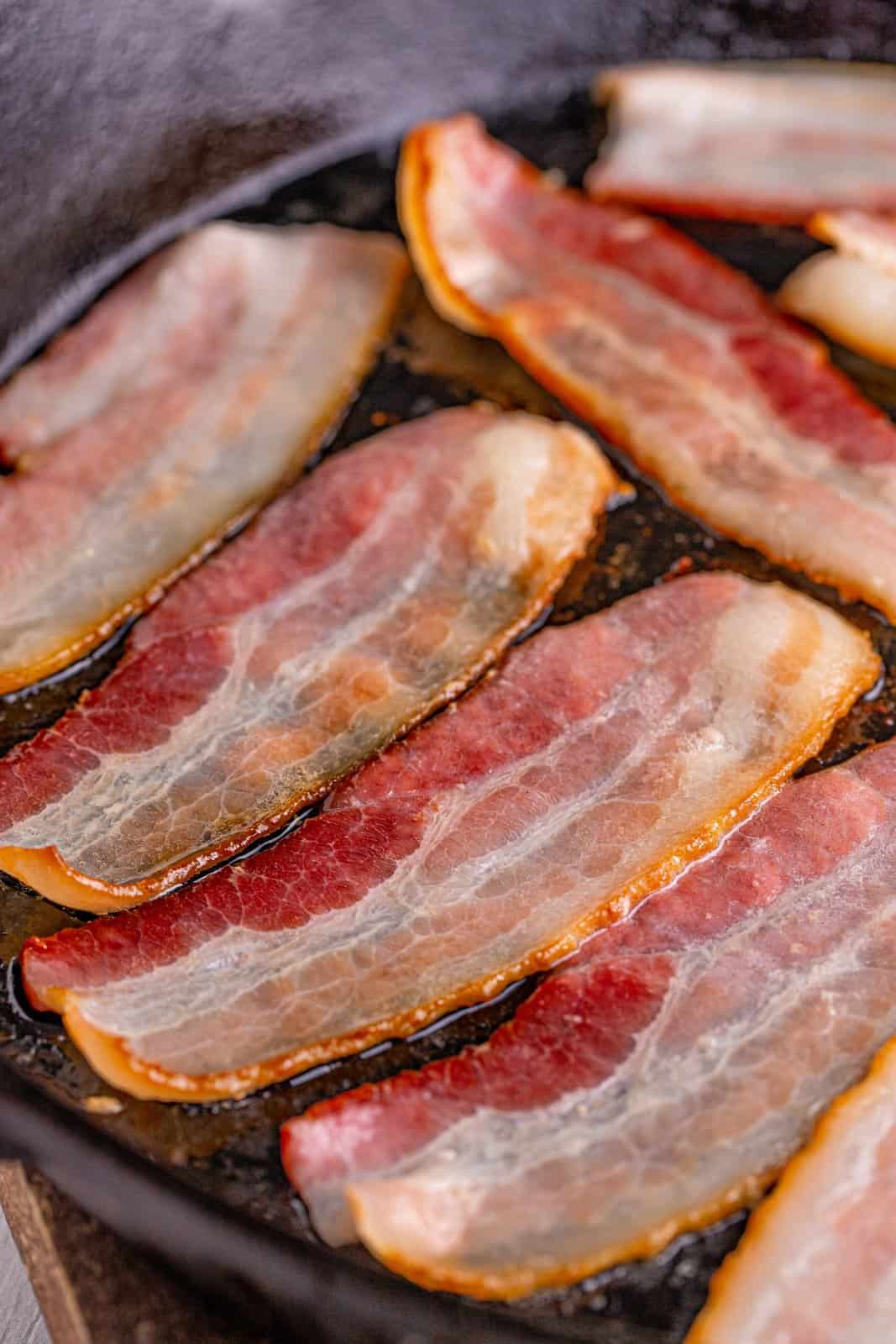 cooking bacon pieces in a cast iron frying pan. 
