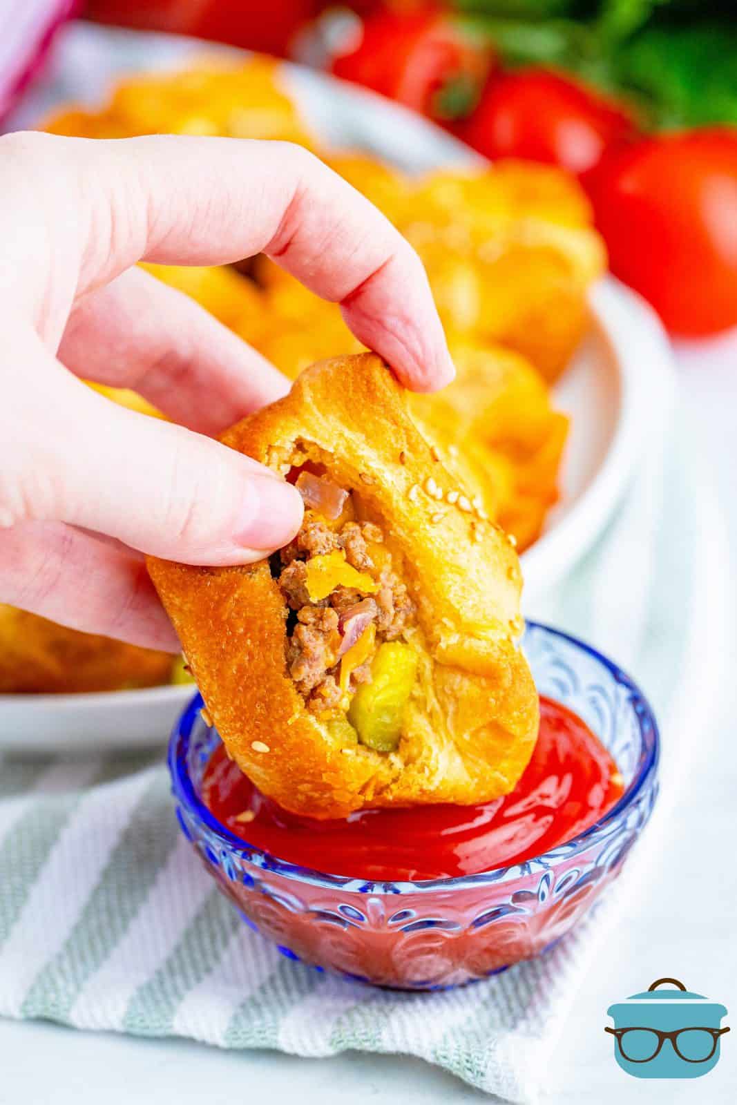 Hand dipping one Easy Cheeseburger Crescent Cup into ketchup.