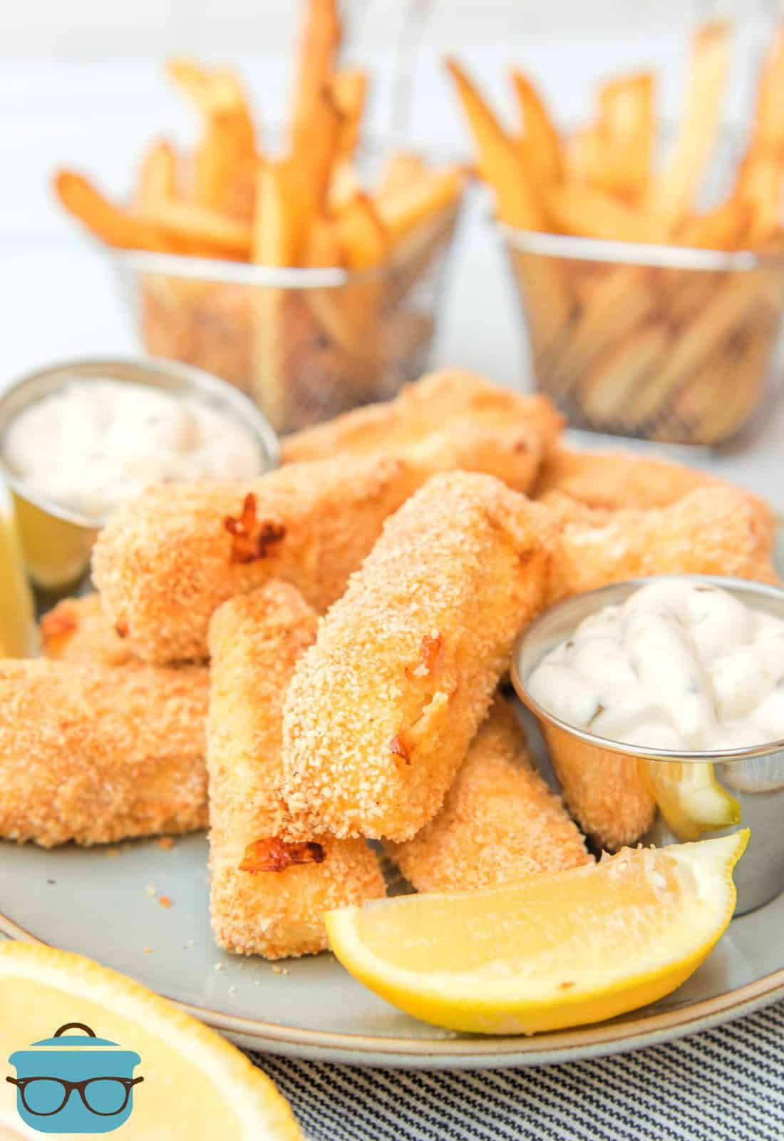 Air Fryer Homemade Fish Sticks stacked with dipping sauce and sliced lemon.