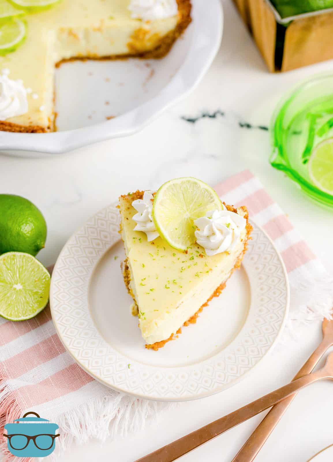 Slice of Key Lime Pie on white plate with whole pie in background